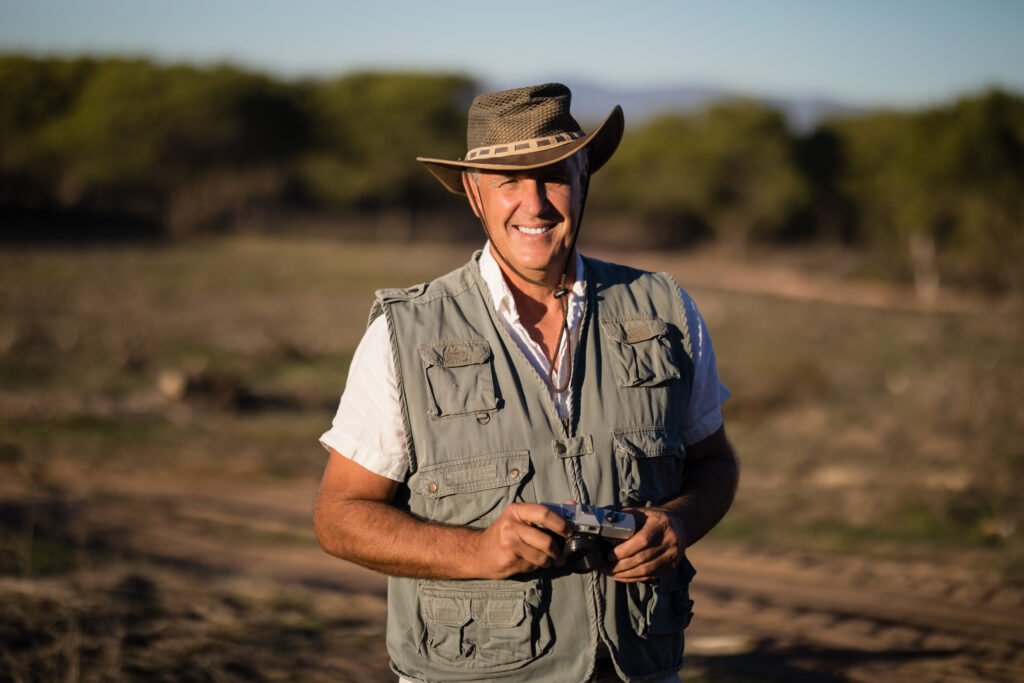 happy man standing with camera during safari vacation on a sunny day